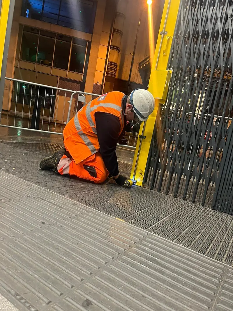 Engineer fitting a yellow collapsible security grille at a station