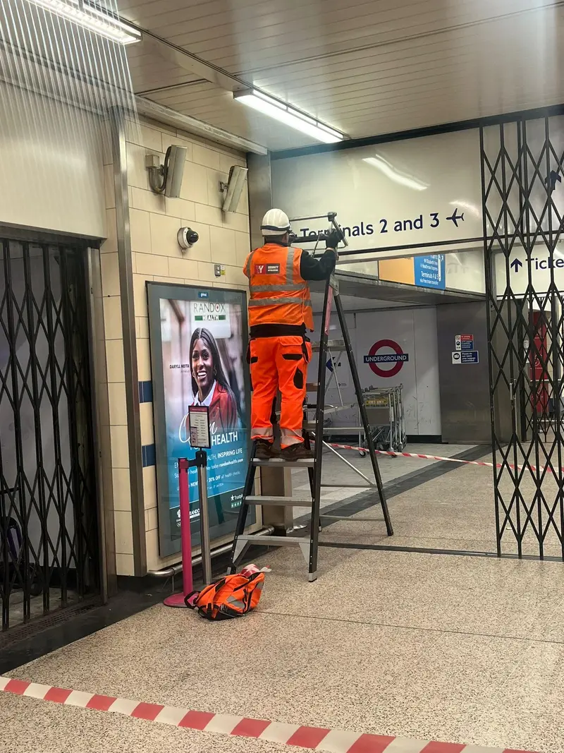 Engineer fitting a grille beneath a Terminals 2 and 3 sign